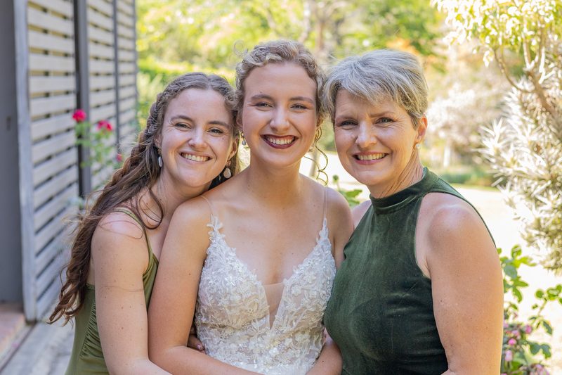 A bride flanked by her sister and mother, all laughing