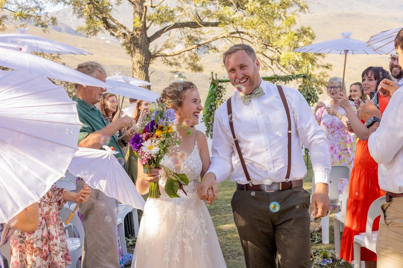 Newlyweds walking back up the aisle through bubbles and paper parasols