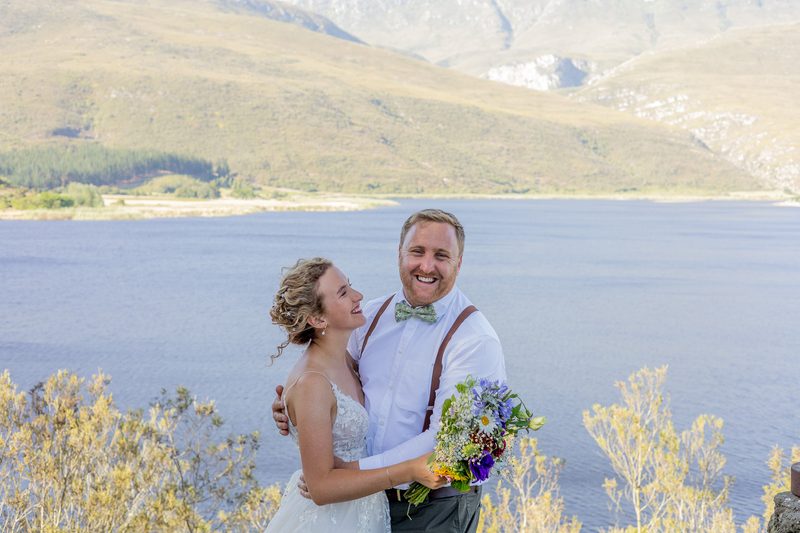 A bride and groom laughing together above a mountain dam