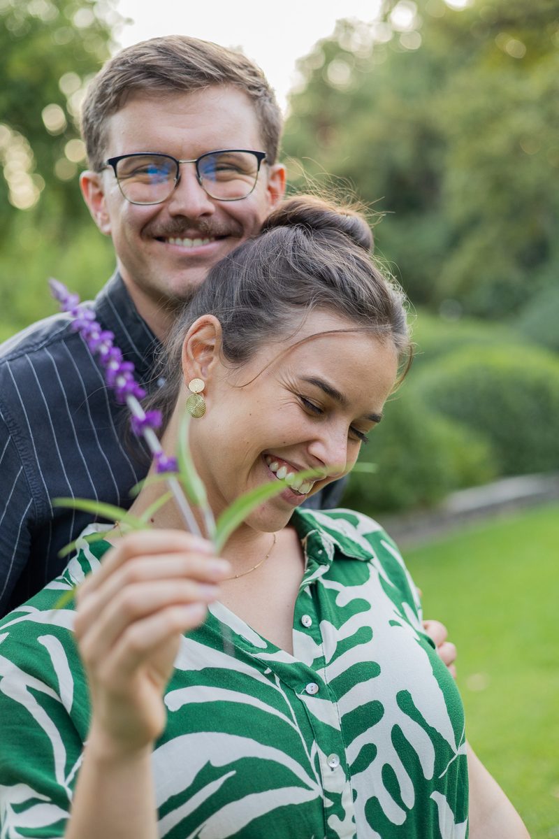 A woman laughing while holding a sprig of lavender, her fiancé behind her