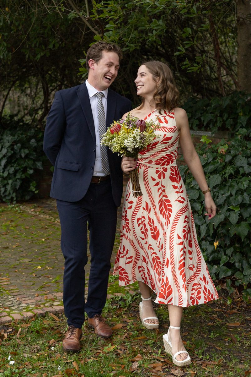 Two guests walking a garden path together, laughing, dressed for a celebration