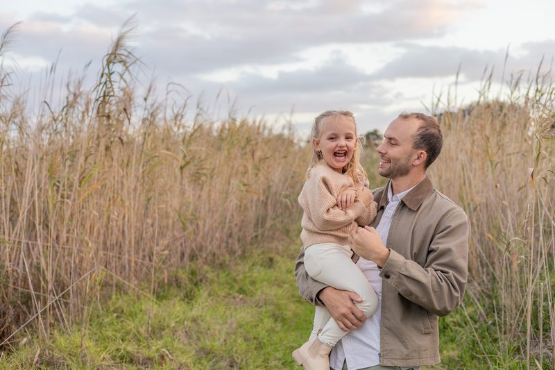 A father laughing with his daughter among the reeds at dusk