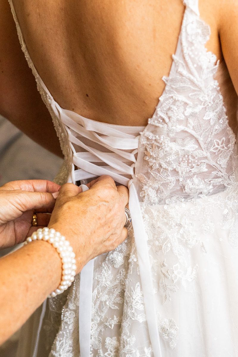Hands lacing the back of a beaded lace wedding dress