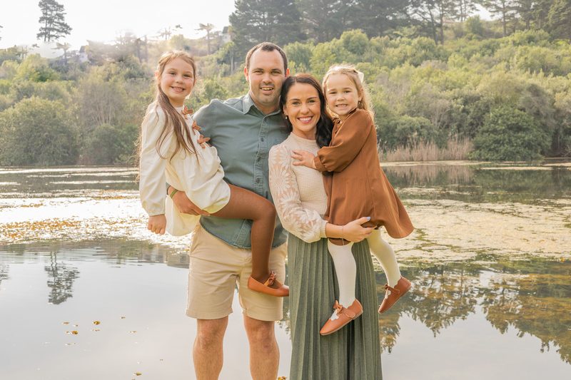 A family of four standing at the edge of a still lake