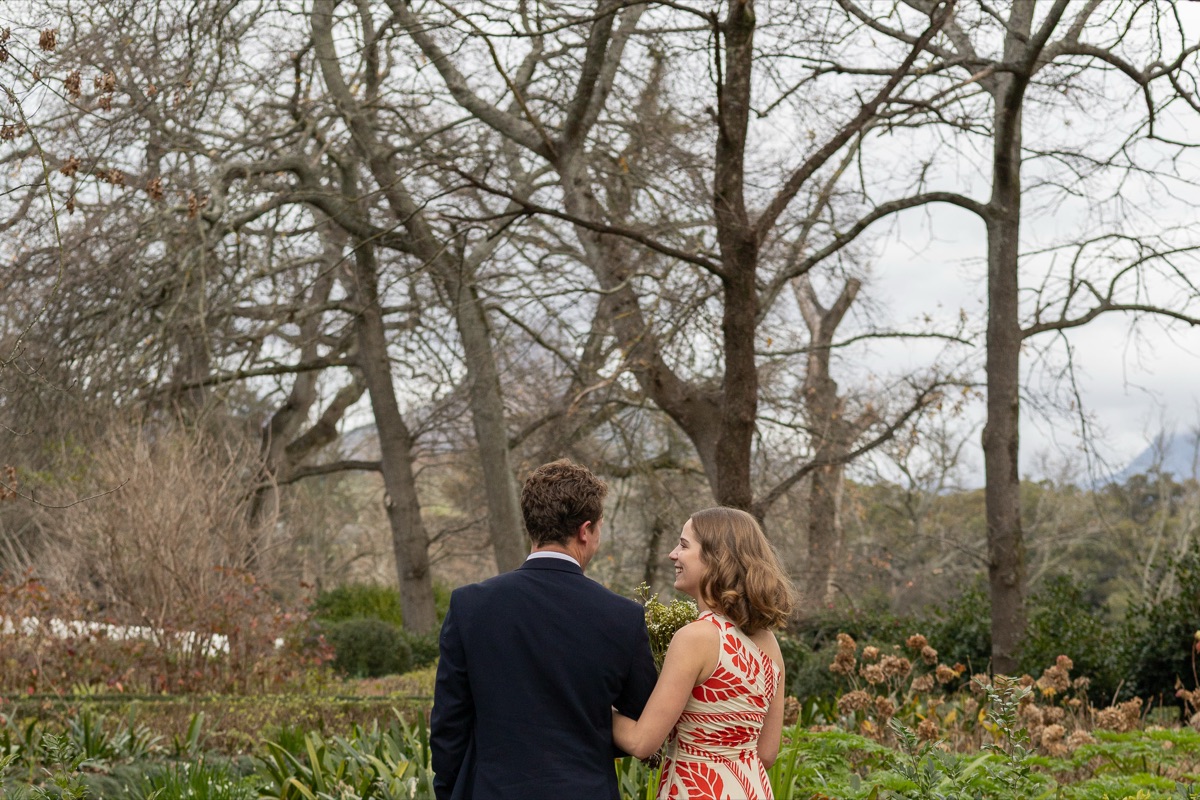 A couple walking together beneath bare winter trees, she looks up at him