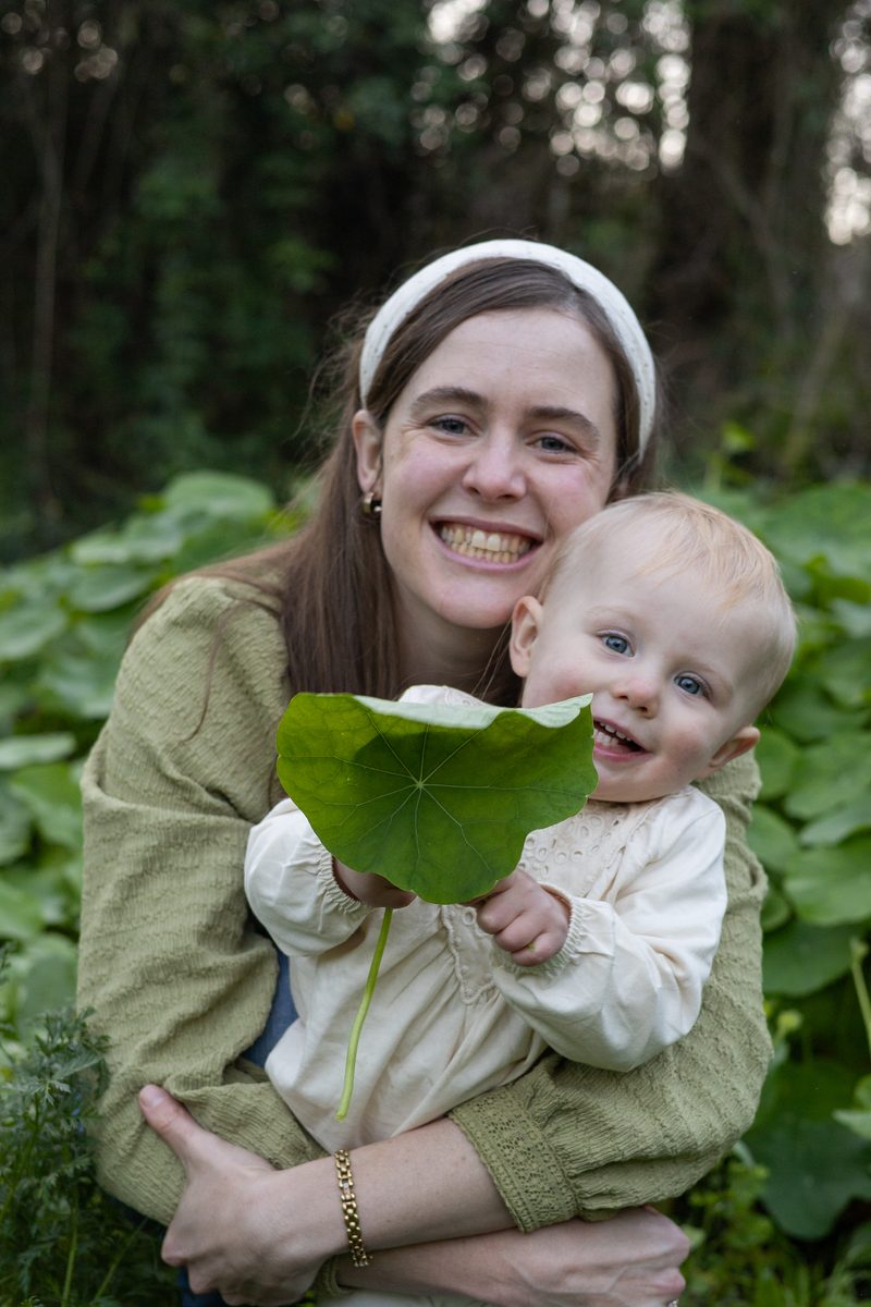 A mother holding her baby, who is holding up a large green nasturtium leaf