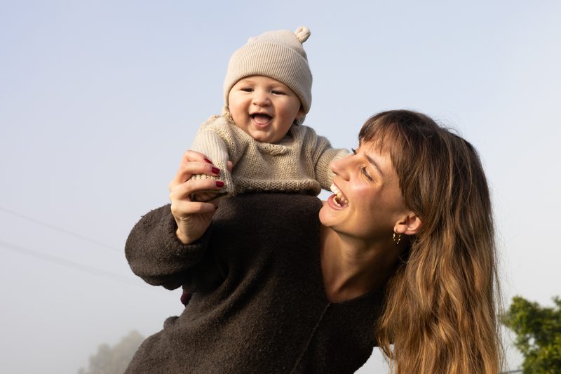 A mother lifting her laughing baby into the morning light