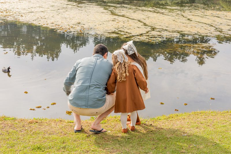 A father and daughter crouched together at the water's edge, watching a bird