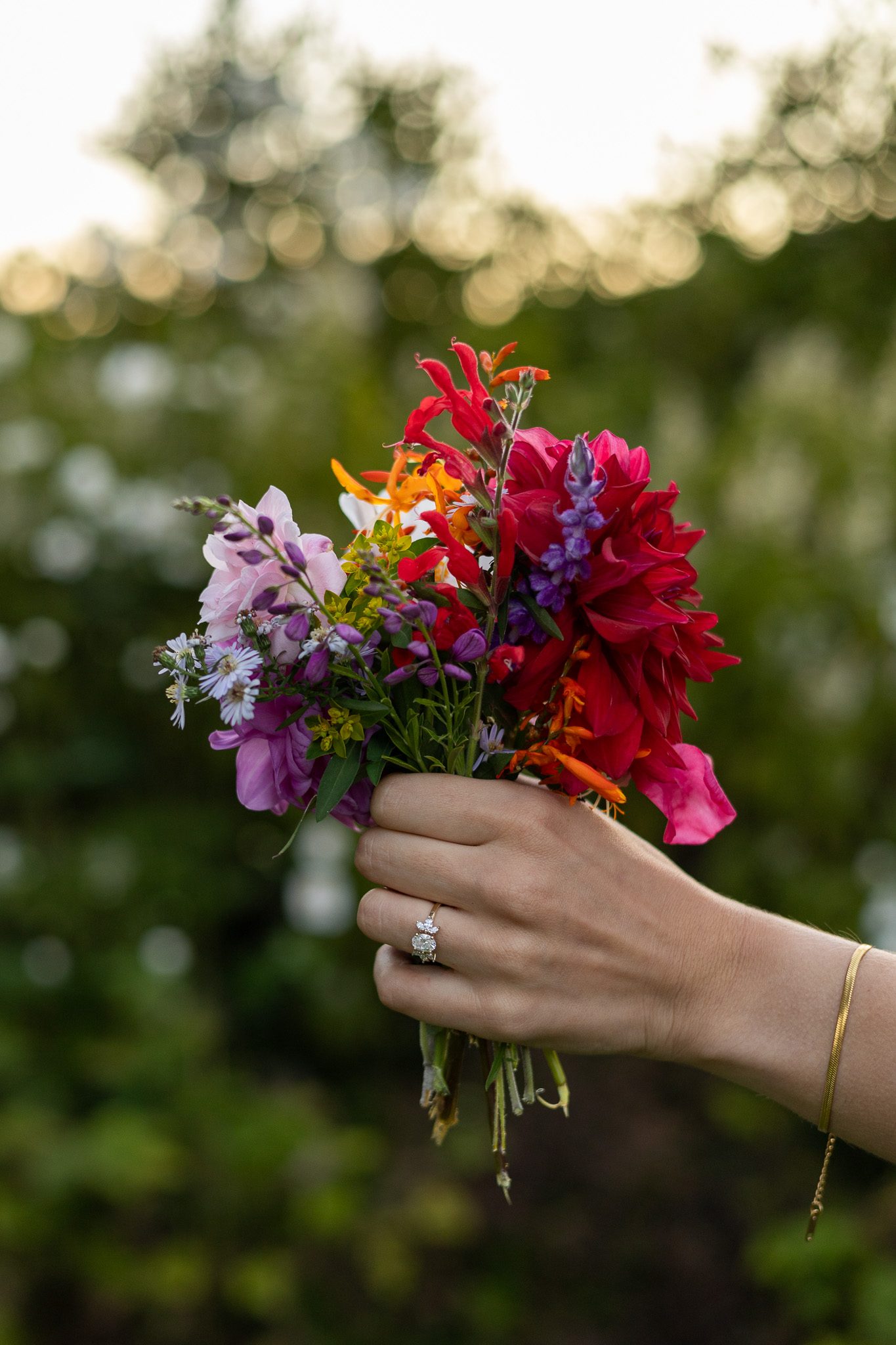 A hand holding a small bouquet of garden flowers, wearing an engagement ring