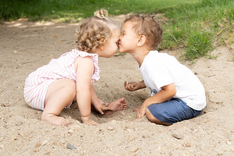 Two toddlers leaning in to kiss while sitting in the sand